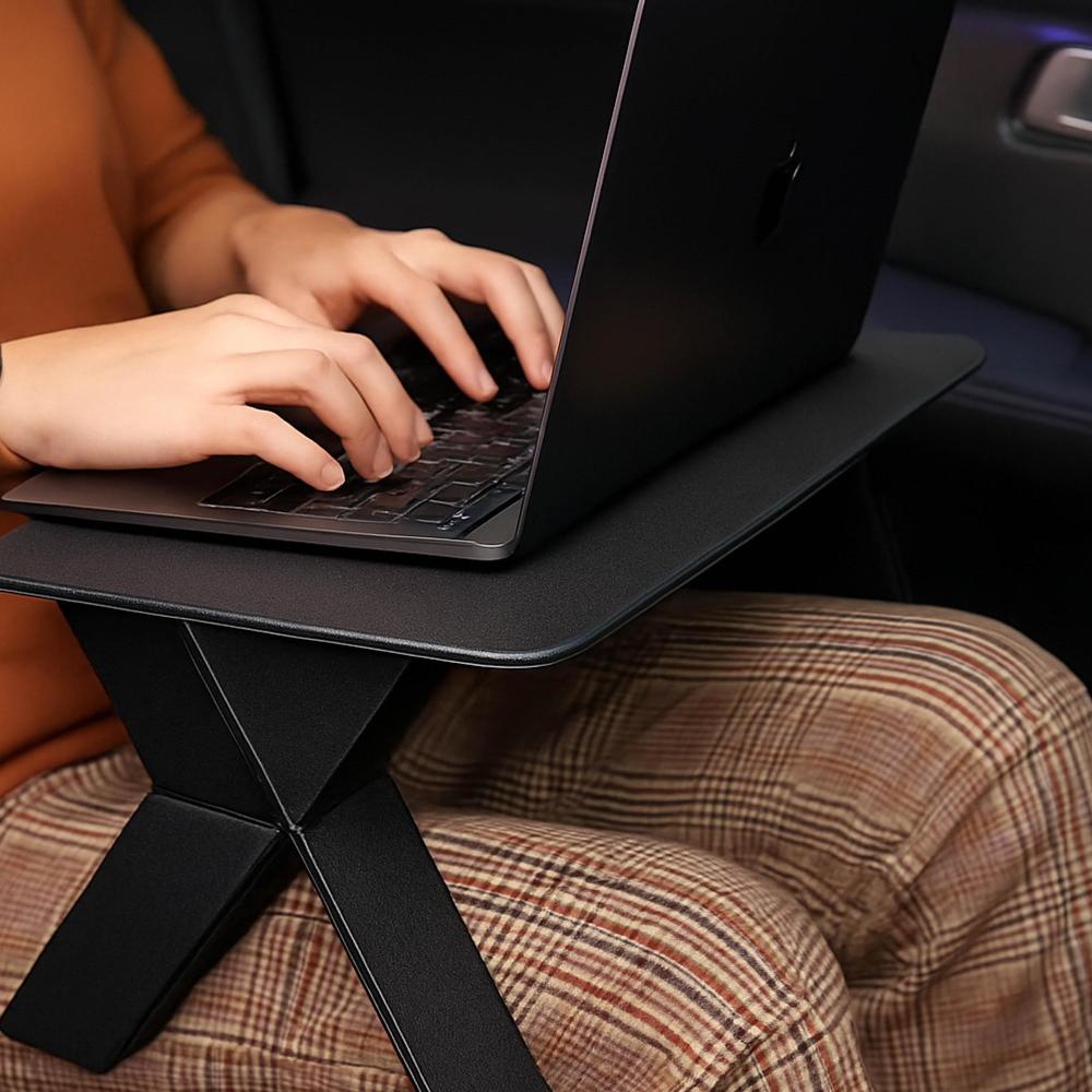 Person using a laptop on a portable black stand in a vehicle.